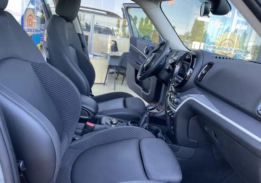 Intérieur avant droit du MINI Countryman F60 hybride, sièges gris noir et tableau de bord moderne avec écran central rond.