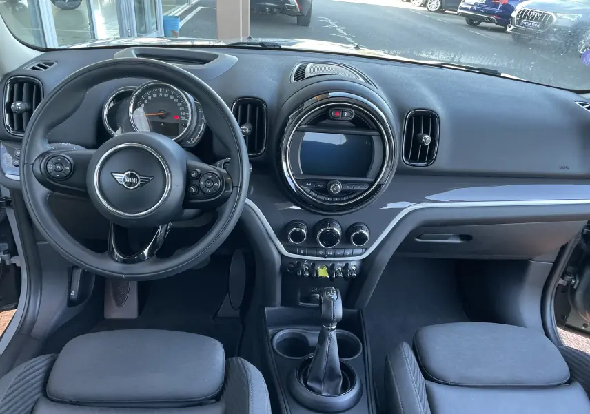 Vue intérieure avant du tableau de bord du MINI Countryman F60 hybride rechargeable en Moonwalk Grey, avec volant multifonction et écran central rond.