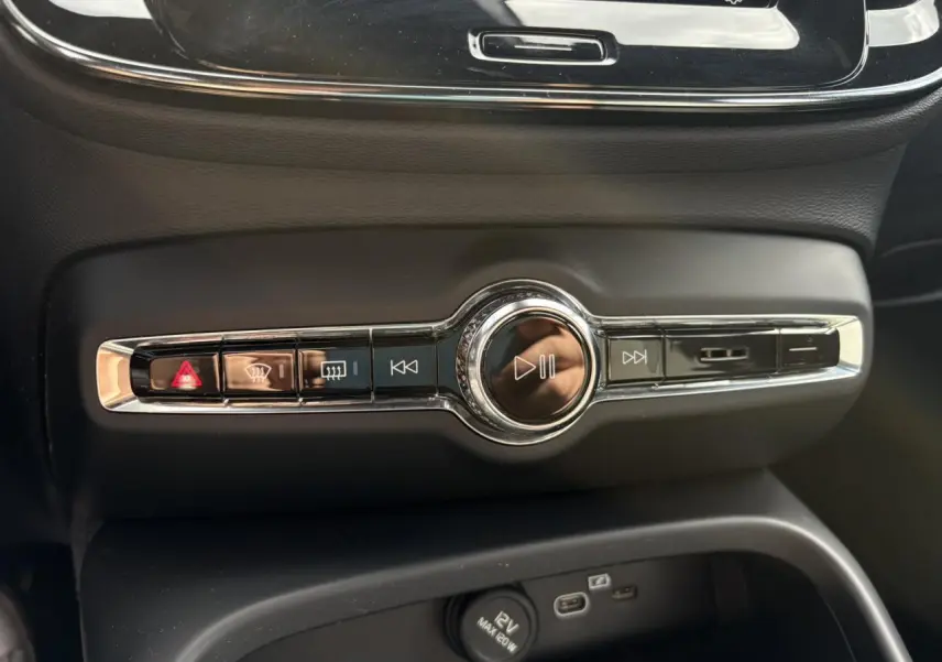 Vue rapprochée des commandes centrales noires et chromées du Volvo XC40 2024, mettant en valeur les boutons multimédia et de sécurité.