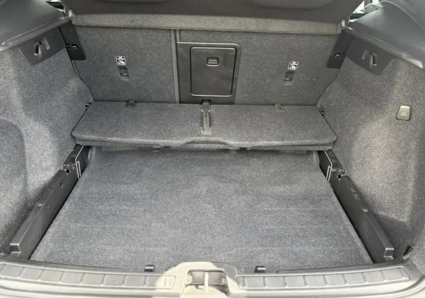 Coffre ouvert du Volvo XC40 B3 MHEV 2024, vue intérieure montrant le plancher et la cloison arrière en tissu gris.