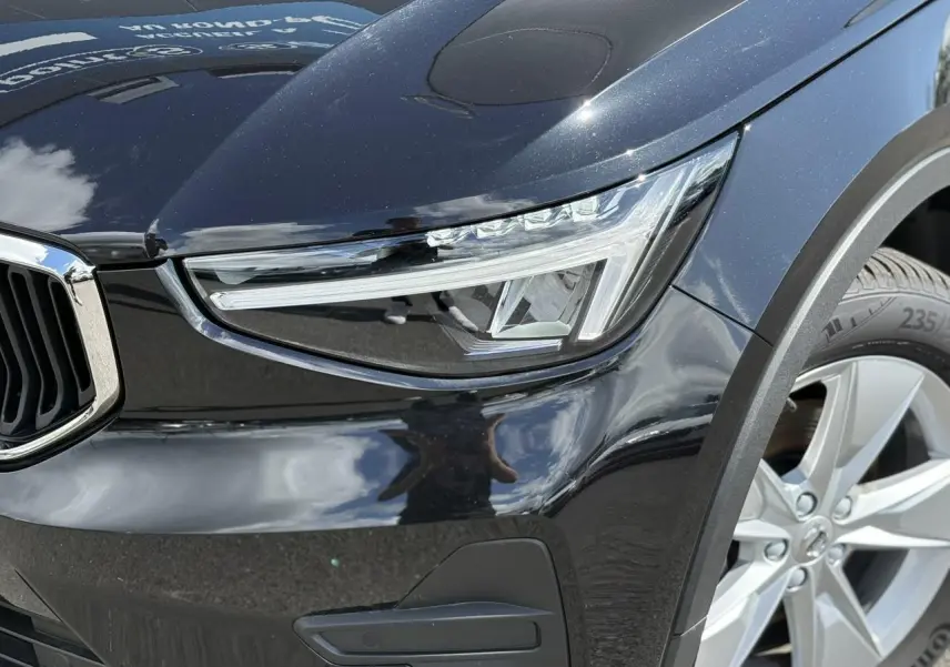 Gros plan sur le phare avant droit et la roue alliage 18'' d'un Volvo XC40 noir Onyx 2024.