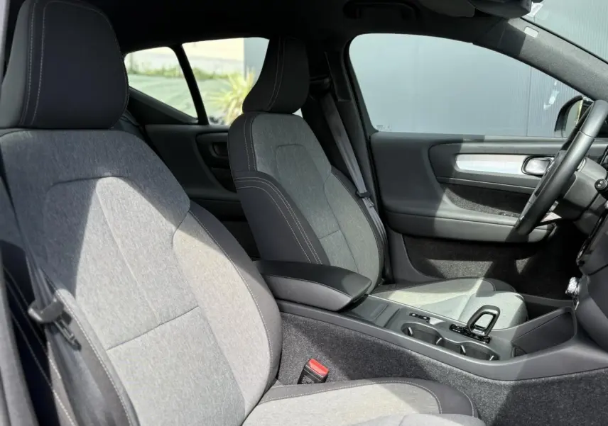 Intérieur du Volvo XC40 2024 vu côté conducteur, sièges tissu gris clair avec surpiqûres blanches et console centrale noire.