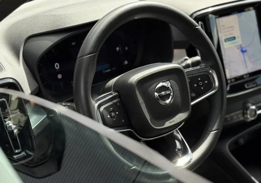 Vue rapprochée du volant noir du Volvo XC40 2024, avec tableau de bord digital et écran tactile central visible.