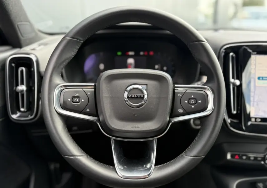 Volant cuir noir avec commandes intégrées du Volvo XC40 2024, tableau de bord et écran tactile visibles en arrière-plan.
