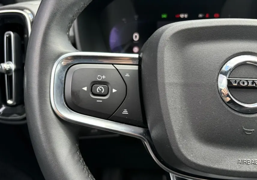 Gros plan sur le volant noir du Volvo XC40 2024, mettant en valeur les commandes de régulateur de vitesse côté gauche.
