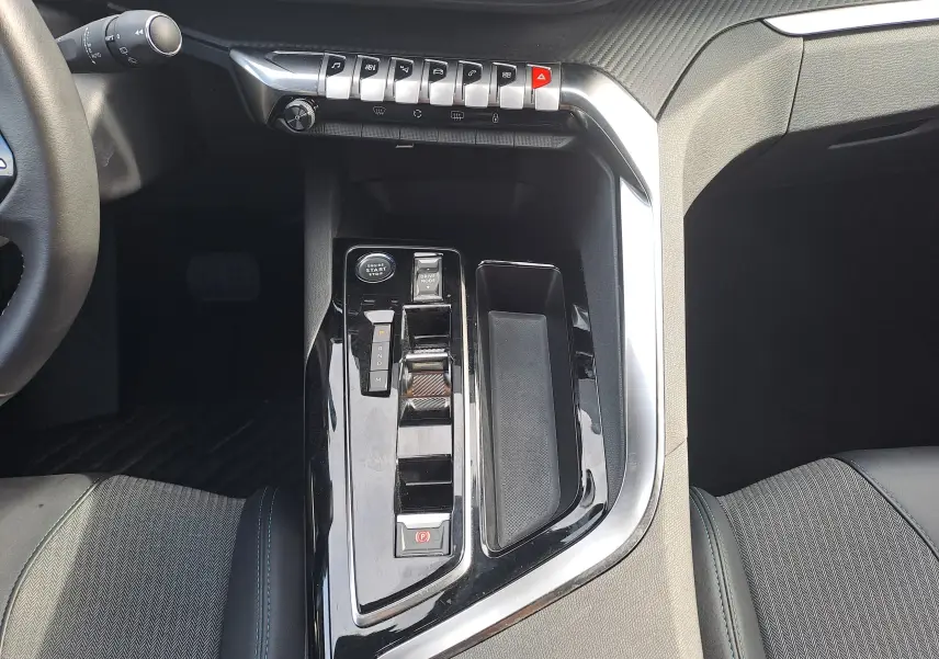 Vue rapprochée de la console centrale noire brillante du Peugeot 3008 Hybrid 145, avec commandes de boîte auto et start/stop.
