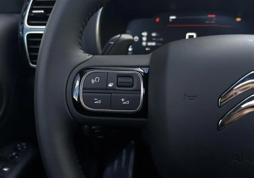 Gros plan sur les commandes gauche du volant noir du Citroën C5 Aircross 2025, avec affichage numérique en arrière-plan.