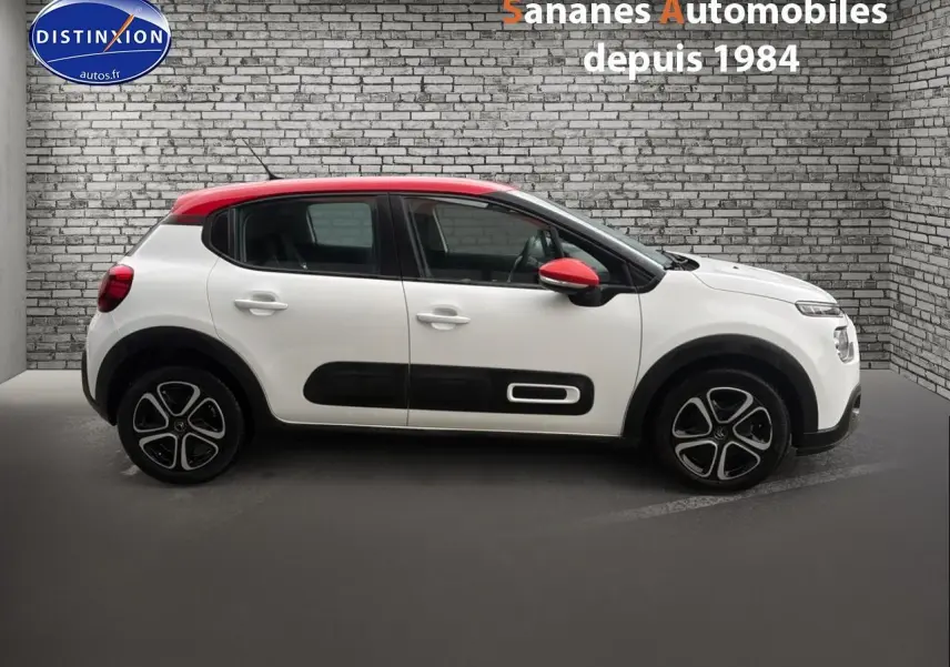 Profil latéral gauche d'une Citroën C3 2021 blanche avec toit et rétroviseurs rouges, enjoliveurs noirs distinctifs.