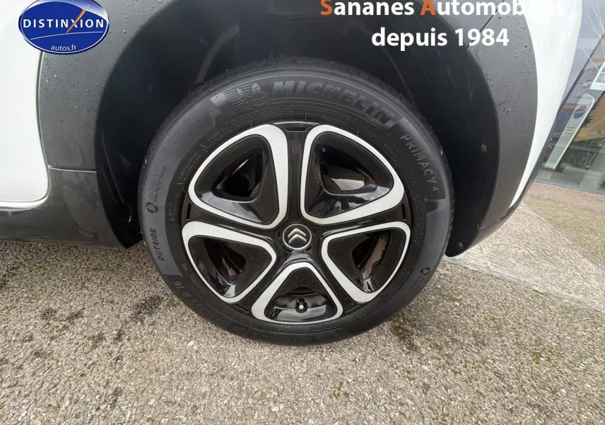 Gros plan sur la roue avant droite d'une Citroën C3 blanc toit rouge avec jante 16 pouces noire et argentée.