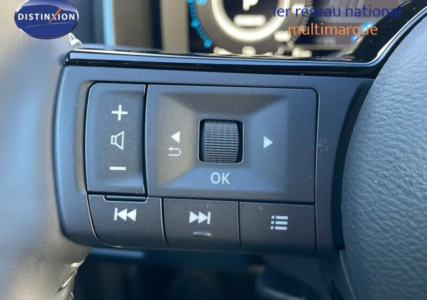 Gros plan sur les commandes au volant du Nissan Qashqai blanc nacré 2025 avec toit noir, affichage digital en arrière-plan.