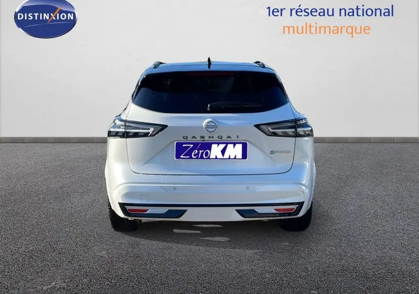 Vue arrière d'un Nissan Qashqai blanc nacré avec toit noir, modèle hybride 2025, affichant ses feux et logo distinctifs.