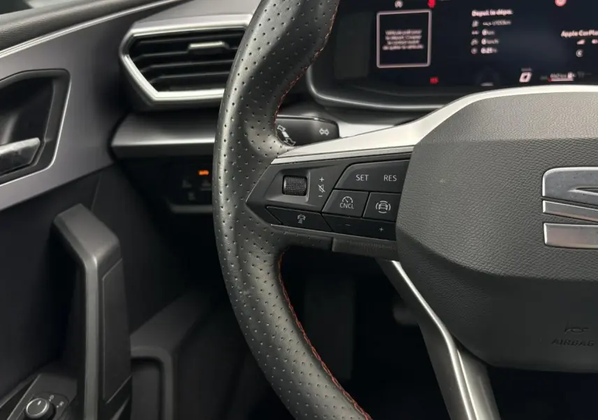 Gros plan sur le volant en cuir perforé avec surpiqûres rouges et commandes multifonctions du SEAT Leon 2025 côté conducteur.
