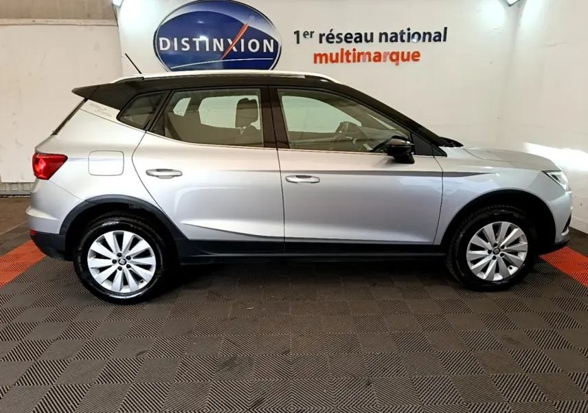 Vue de profil côté gauche d'un SEAT Arona gris clair avec toit noir, dans un showroom intérieur.