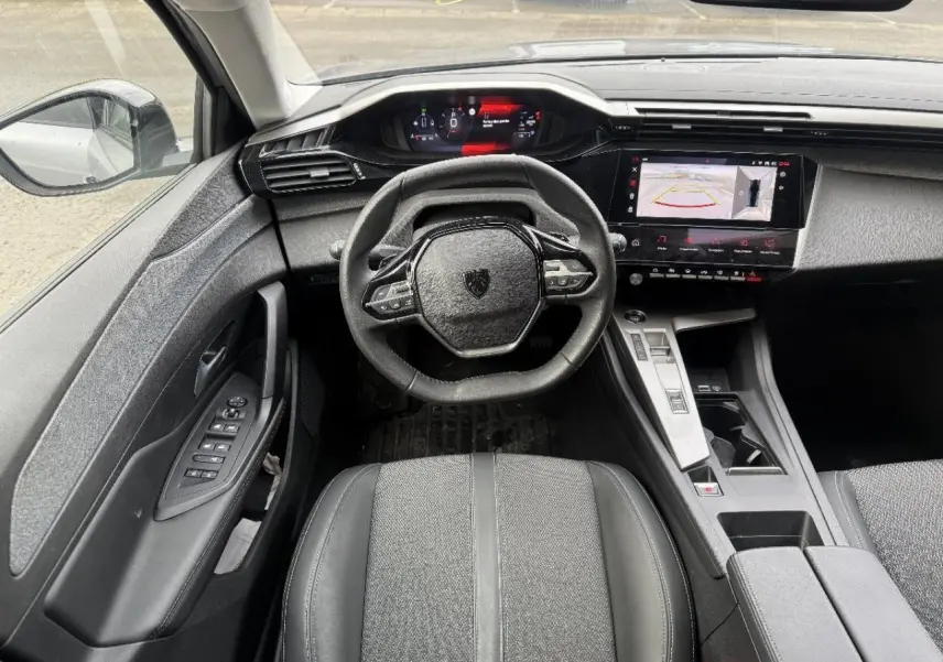 Vue intérieure centrée sur le poste de conduite de la Peugeot 308 gris sellenium, avec volant compact et écran tactile.