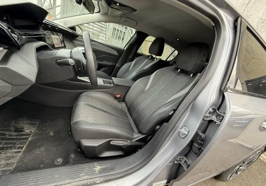 Intérieur de la Peugeot 308 1,2 Hybrid 2025 vu côté conducteur, sièges tissu et cuir gris, tableau de bord moderne.