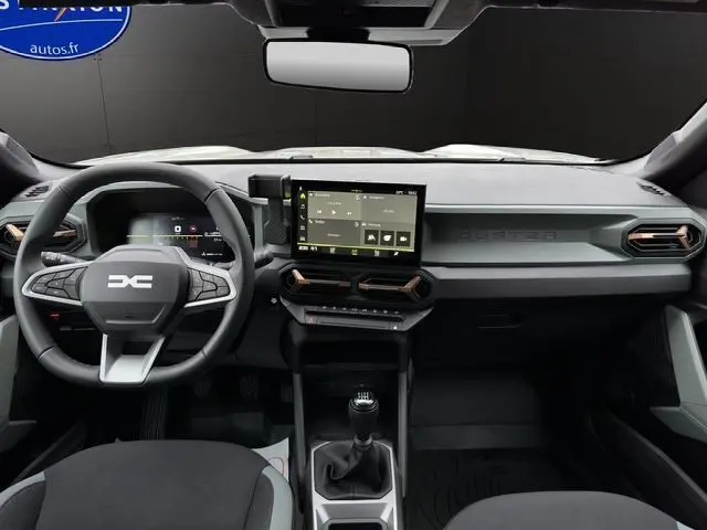 Intérieur noir du Dacia Duster 2025, vue frontale sur tableau de bord avec écran tactile et volant multifonction.