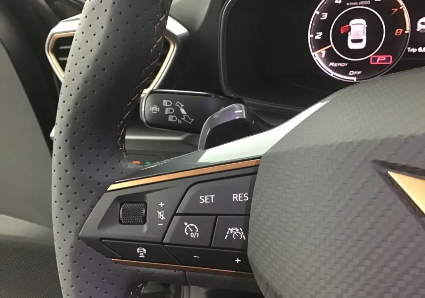 Gros plan sur le volant perforé noir de la CUPRA Leon 2023, avec commandes de régulateur et tableau de bord digital visible.
