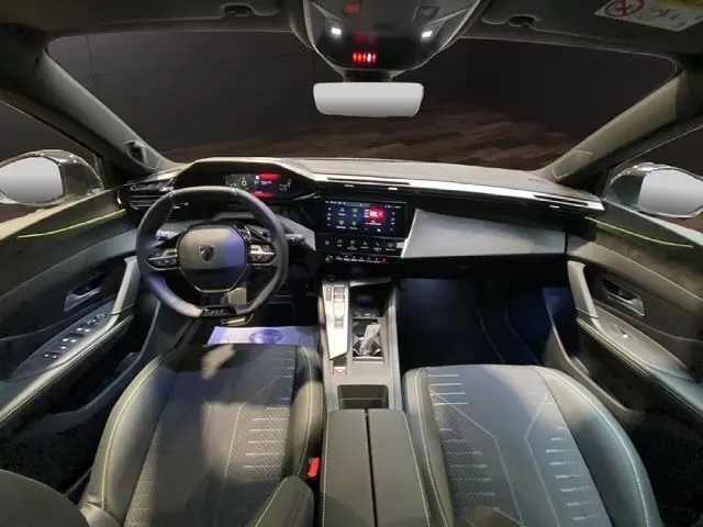 Vue intérieure avant de la Peugeot 308 hybride 2026, avec tableau de bord numérique et sièges noirs en tissu et cuir.