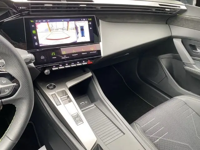 Vue intérieure côté passager de la Peugeot 308 hybride blanche, avec écran tactile affichant la caméra de recul et console moderne.