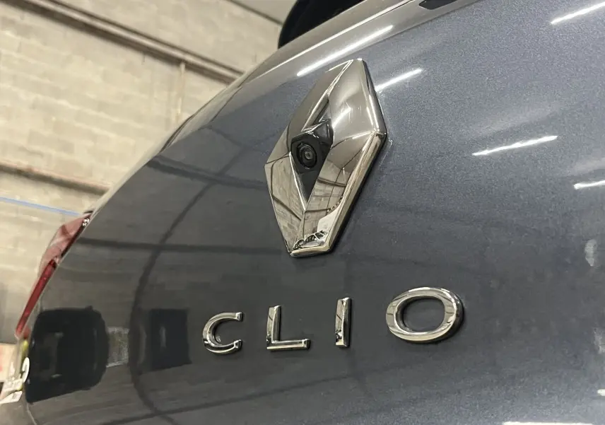 Gros plan sur le logo Renault et l’inscription Clio à l’arrière d’une Renault Clio V gris titanium dans un garage.