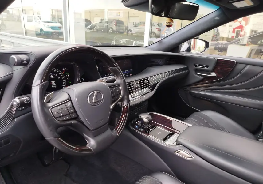 Vue intérieure côté conducteur de la Lexus LS 500H 2020 avec tableau de bord noir et inserts bois foncé.