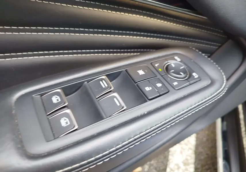 Gros plan sur les commandes de vitres et rétroviseurs sur la porte en cuir noir avec surpiqûres blanches d'une Lexus LS 500H.