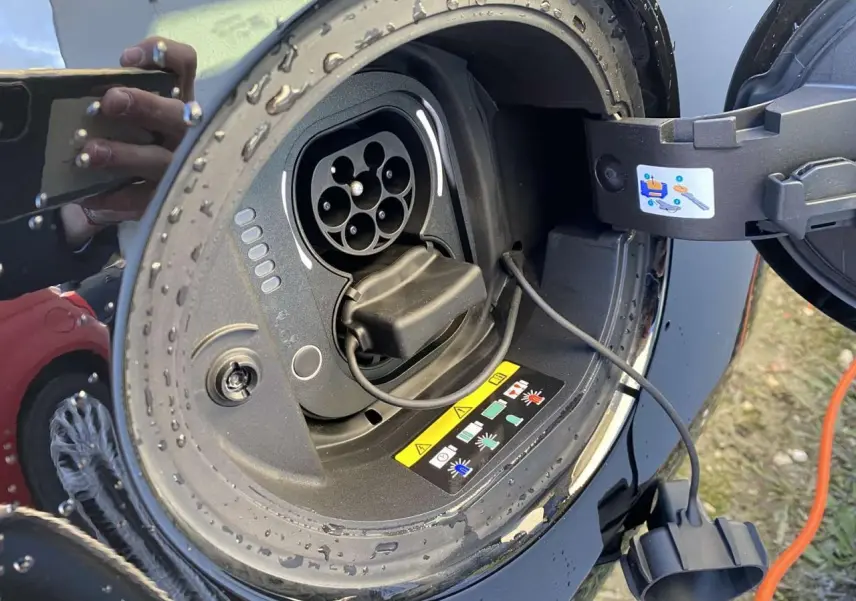 Prise de recharge électrique ouverte sur une FIAT 500 noire, avec câble de charge visible et gouttes d'eau.