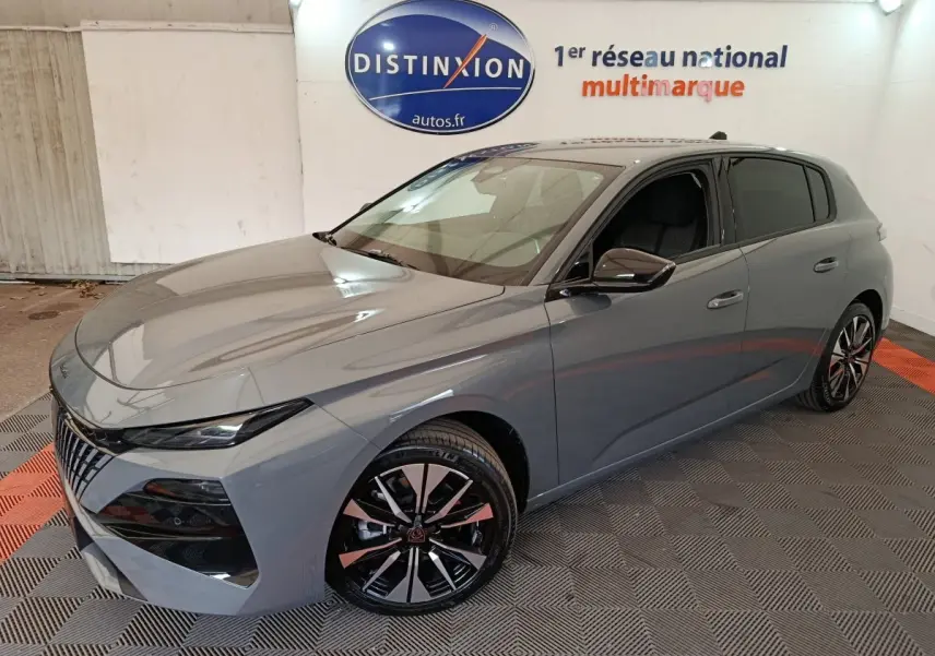 Peugeot 308 gris foncé vue 3/4 avant droit, avec jantes alliage noires et vitres teintées, en intérieur showroom.