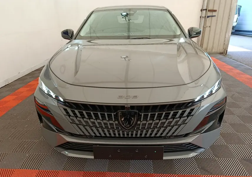 Vue avant frontale d'une Peugeot 308 gris foncé avec calandre distinctive et phares LED fins dans un garage.