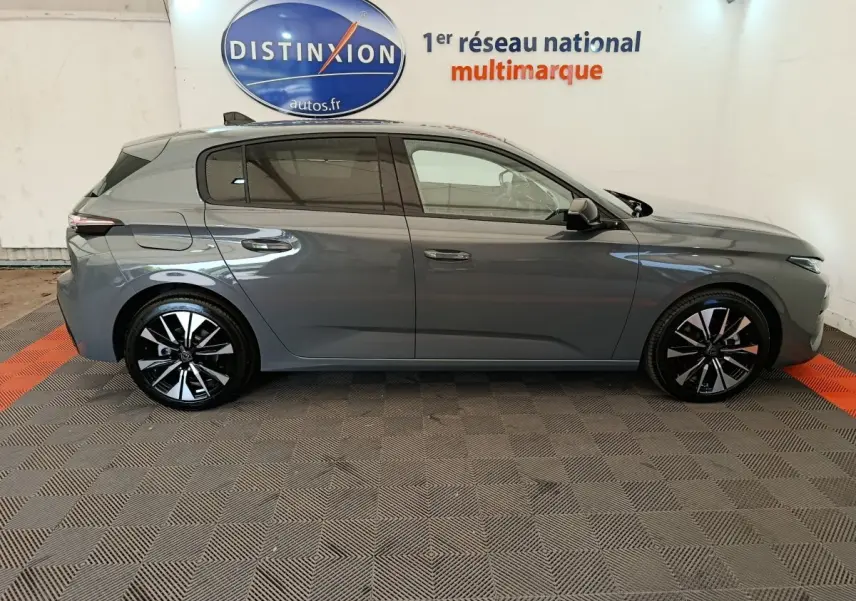 Profil côté droit d'une Peugeot 308 gris foncé 2026 avec jantes noires et détails chromés, en intérieur showroom.