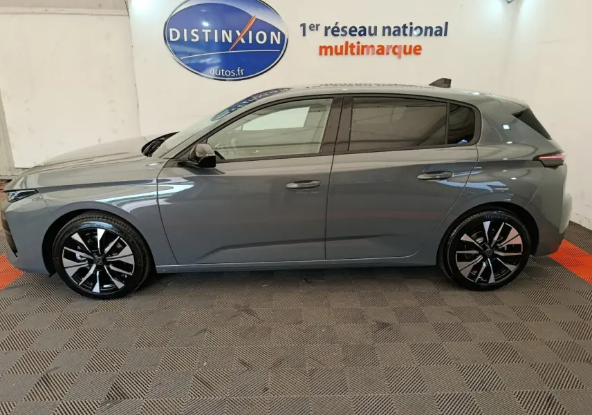 Profil côté gauche d'une Peugeot 308 gris foncé 2026 avec jantes noires et logo Distinxion en arrière-plan.