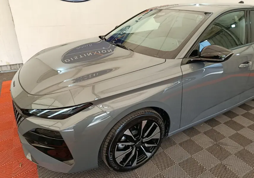 Vue 3/4 avant droit d'une Peugeot 308 gris foncé 2026 avec jantes noires et phares LED fins.