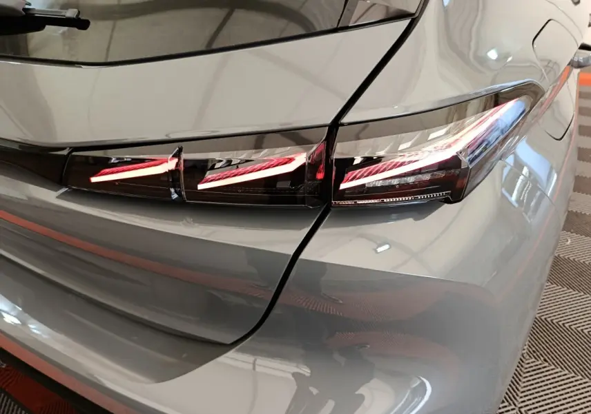 Feu arrière droit allumé sur Peugeot 308 gris foncé, vue rapprochée du coin arrière du véhicule.