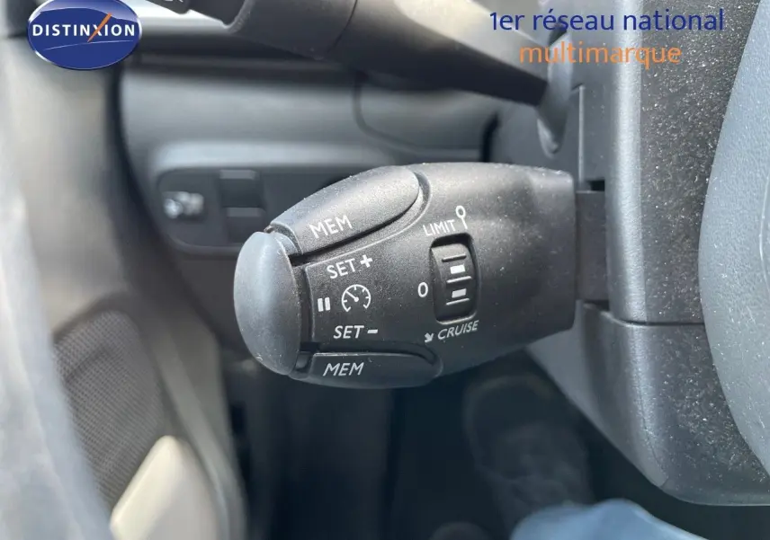Gros plan sur la commande de régulateur de vitesse à gauche du volant dans l'habitacle d'une Citroën C3 gris platinium.