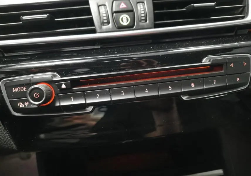 Gros plan sur la commande radio noire avec boutons numérotés et molette rouge dans l'habitacle d'une BMW Série 2 Gran Tourer blanche.