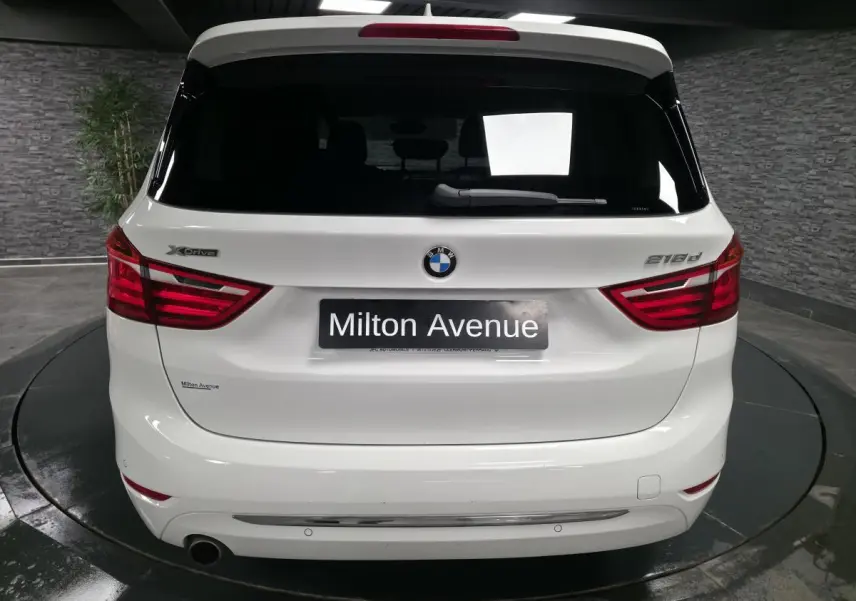 Vue arrière d'une BMW Série 2 Gran Tourer blanche avec badges xDrive et 218d dans un showroom.