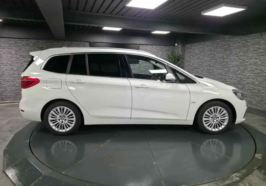 BMW Série 2 Gran Tourer blanc vue de profil côté gauche avec jantes alliage 17 pouces en intérieur showroom.