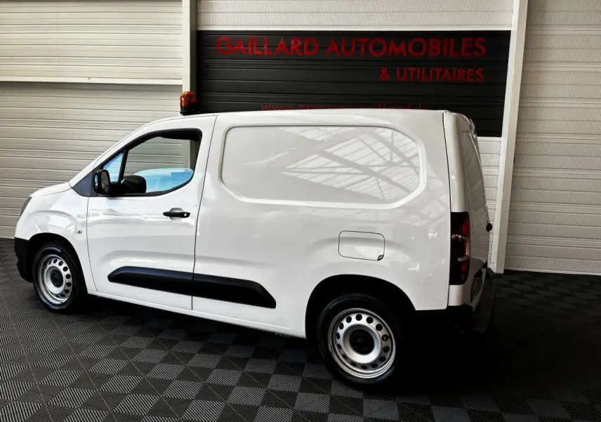 Vue de profil côté gauche d'un utilitaire Opel Combo blanc avec cloison pleine et jantes acier en intérieur showroom.