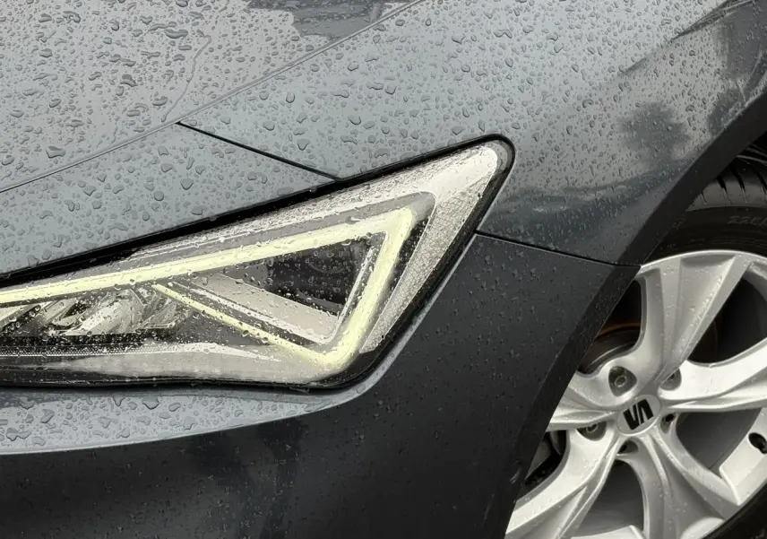 Gros plan sur le phare avant gauche et la jante alliage 17'' d'une SEAT LEON Gris Magnétique sous la pluie.