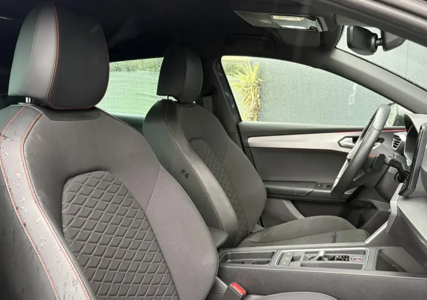 Vue intérieure côté droit du SEAT LEON 2024 FR avec sièges tissu noir à surpiqûres rouges et ciel de toit noir.