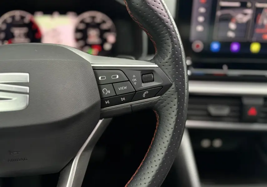 Gros plan sur le volant cuir perforé avec surpiqûres rouges du SEAT LEON 2024, boutons multifonctions visibles côté droit.