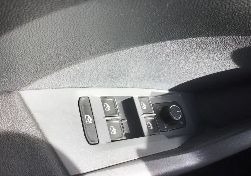 Gros plan sur les commandes des vitres électriques et rétroviseurs chauffants côté conducteur d’un Volkswagen T-Cross blanc.