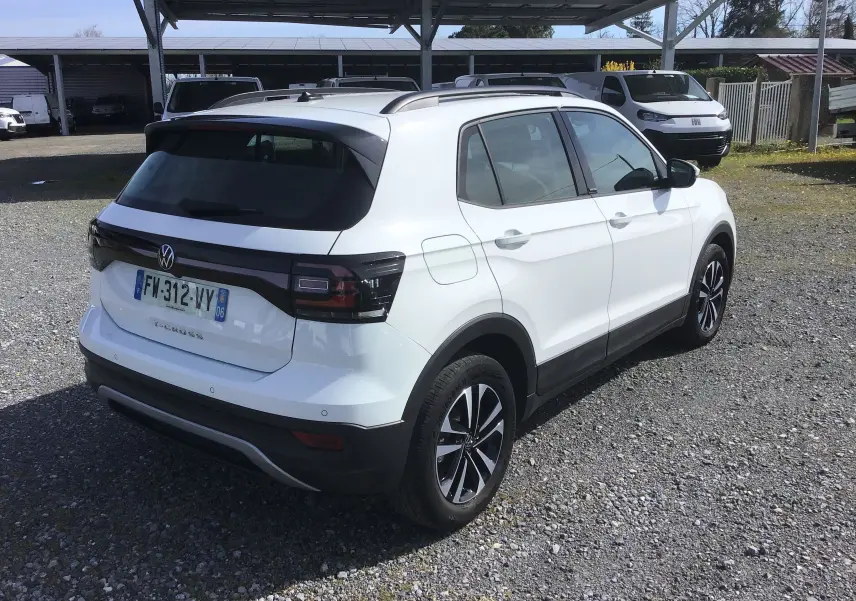 Vue 3/4 arrière droite d'un Volkswagen T-Cross blanc 2021 avec jantes alliage noires et feux arrière foncés.