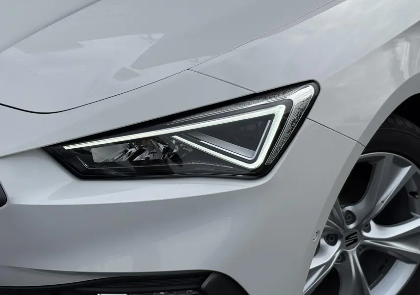 Gros plan sur le phare avant droit et la jante alliage 17 pouces d'une SEAT Leon blanche 2024 finition FR.