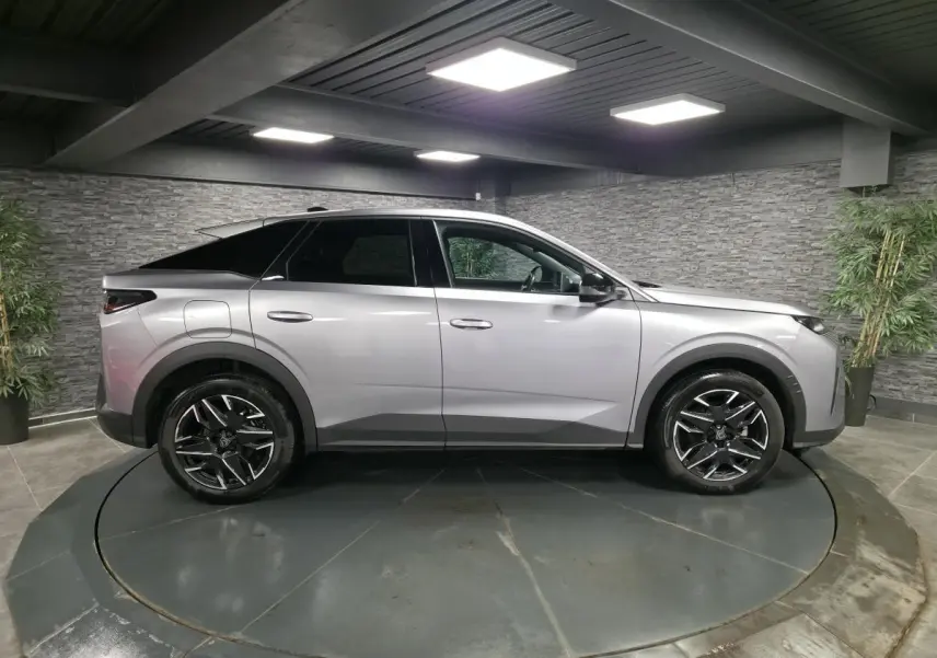 Vue latérale droite d’un Peugeot 3008 gris métallisé 2025 avec jantes alliage noires et toit noir dans un showroom.