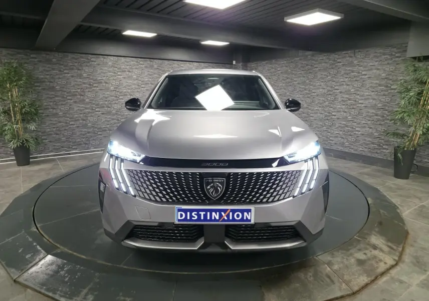 Vue frontale d'un Peugeot 3008 gris métallisé avec calandre noire laquée et feux LED allumés dans un showroom.