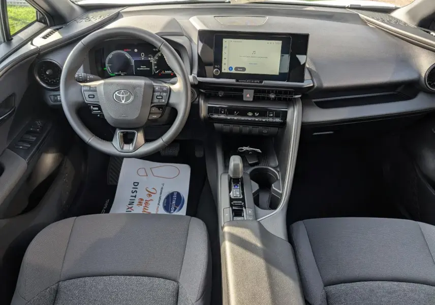 Vue intérieure avant du Toyota C-HR 2024 hybride, tableau de bord avec écran tactile 8 pouces et volant multifonctions.