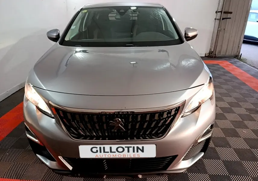 Vue avant d'un Peugeot 5008 gris clair 2020 avec calandre noire et phares allumés en intérieur showroom.