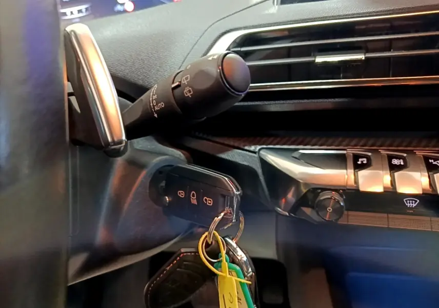 Gros plan intérieur sur la colonne de direction et le tableau de bord noir du Peugeot 5008 avec clé insérée et commandes tactiles visibles.