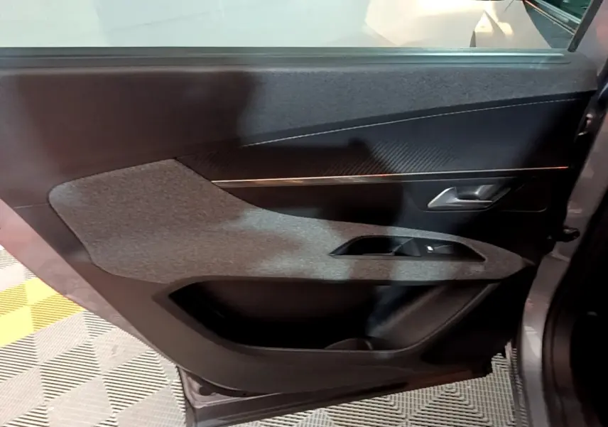 Porte arrière droite ouverte de Peugeot 5008 gris clair, avec habillage tissu et plastique noir, poignée argentée visible.